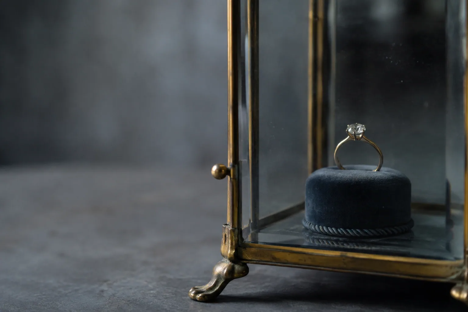 A diamond solitaire ring on a velvet stand inside an antique glazed vitrine with aged brass fittings