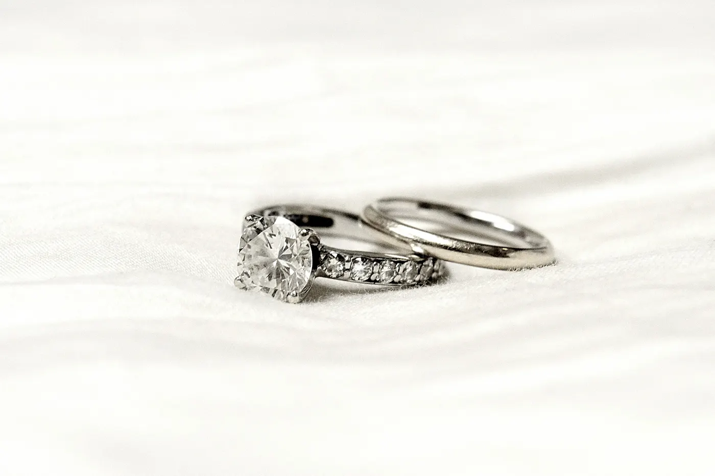 An engagement ring with a channel set band of equal sized diamonds, beside a plain wedding band on white fabric