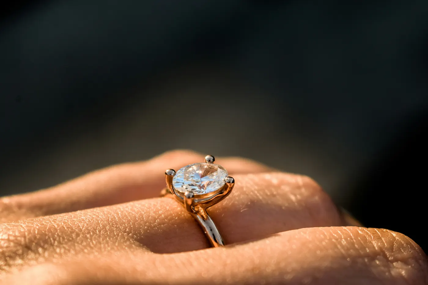 A four claw solitaire engagement ring in yellow gold, worn on the hand in low sunlight