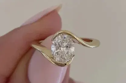 A tension style setting in yellow gold, the band sweeping around an oval stone that appears to float